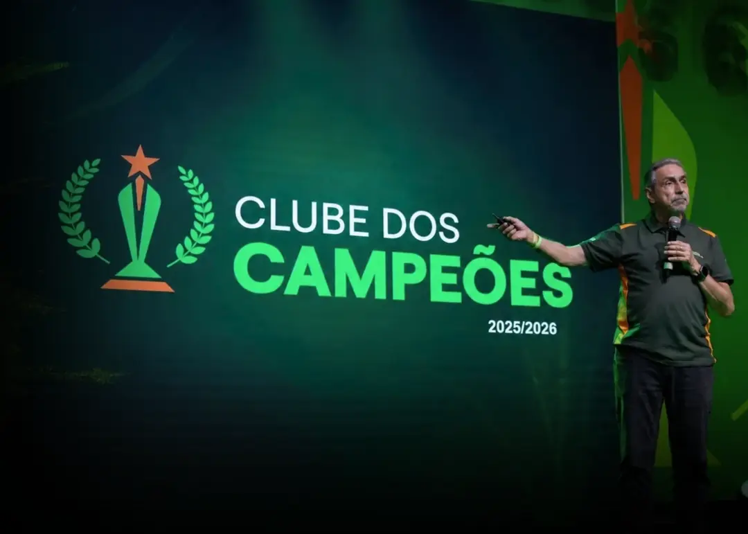 Palestrante no palco do Clube dos Campeões, com o troféu do evento no telão verde