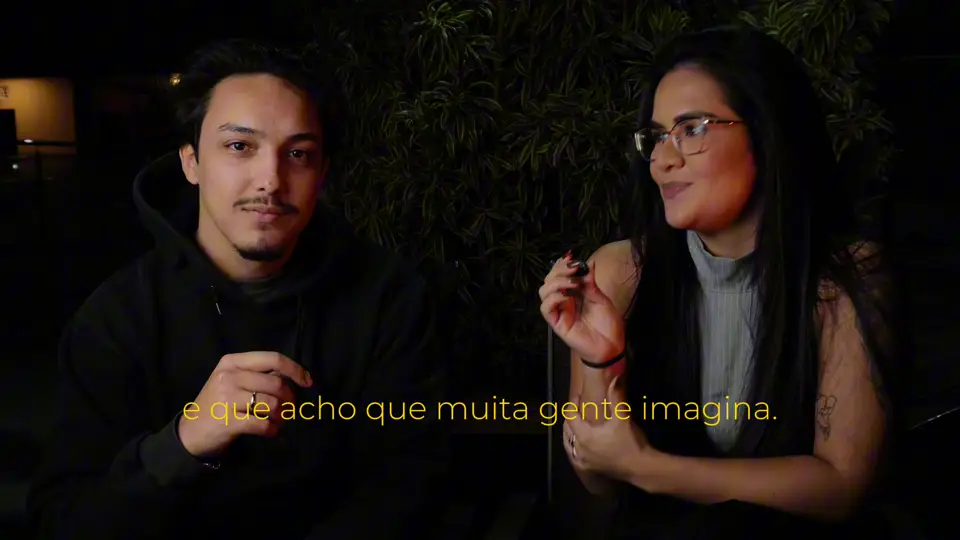 Thaís conversa com o entrevistador num fundo escuro com plantas