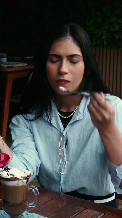Mulher prova o chocolate quente com chantilly numa mesa de madeira
