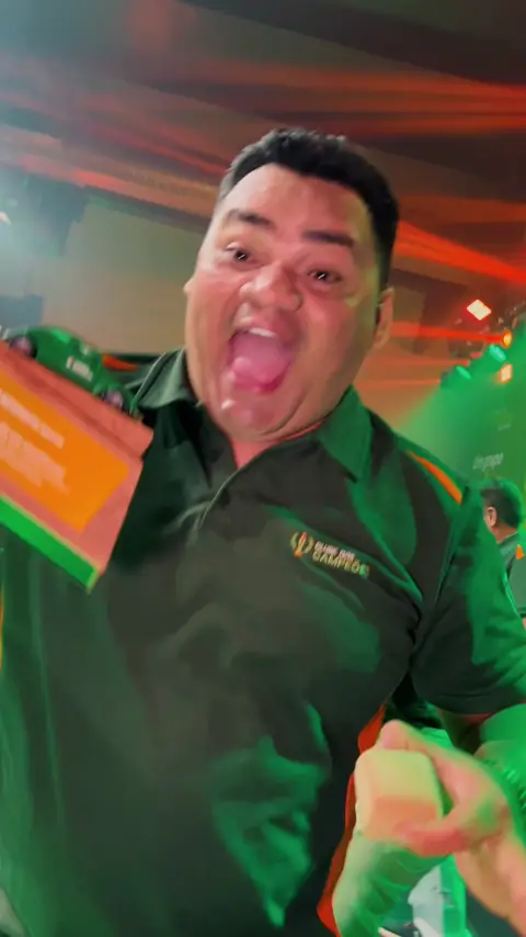 Premiado de camisa verde comemora com o prêmio na mão, sob luzes vermelhas e verdes